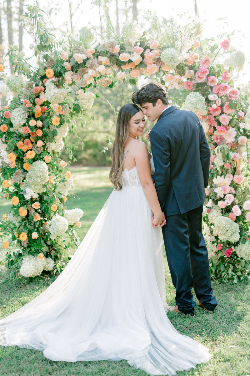BRIDE AND GROOM OUTDOOR WEDDING PORTRAITS IN FRONT OF FLORAL CEREMONY ARCH