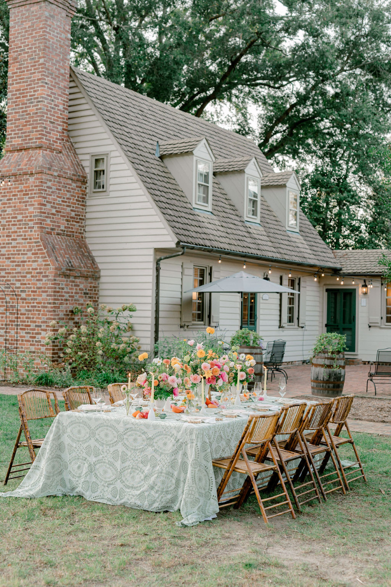 A WEDDING TABLESCAPE WITH CITRUS FLOWER ARRANGEMENTS SET UP OUTSIDE A COUNTRY HOME