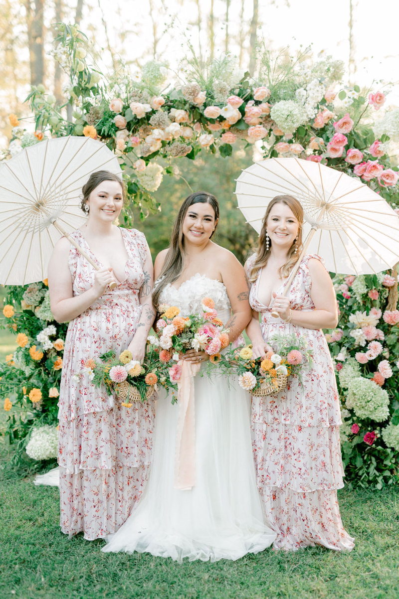 BRIDE WITH BRIDESMAIDS OUTDOOR WEDDING PORTRAITS IN FRONT OF FLORAL CEREMONY ARCH