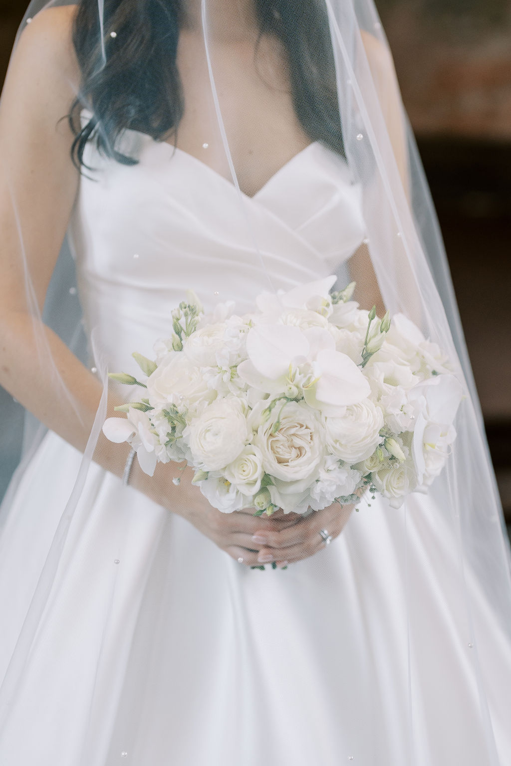 Bride in a strapless satin gown holding a classic white bouquet with roses and orchids, partially covered by a pearl-dotted veil.

when to send bachelorette party invitations