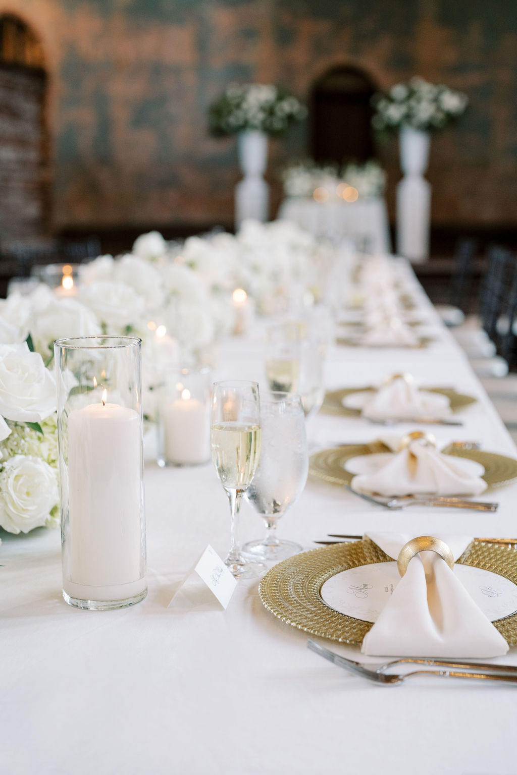 Elegant reception table with white roses, candlelight, champagne glasses, and gold chargers. A luxurious and polished tablescape perfect for a sophisticated wedding celebration. -- wedding guest list template