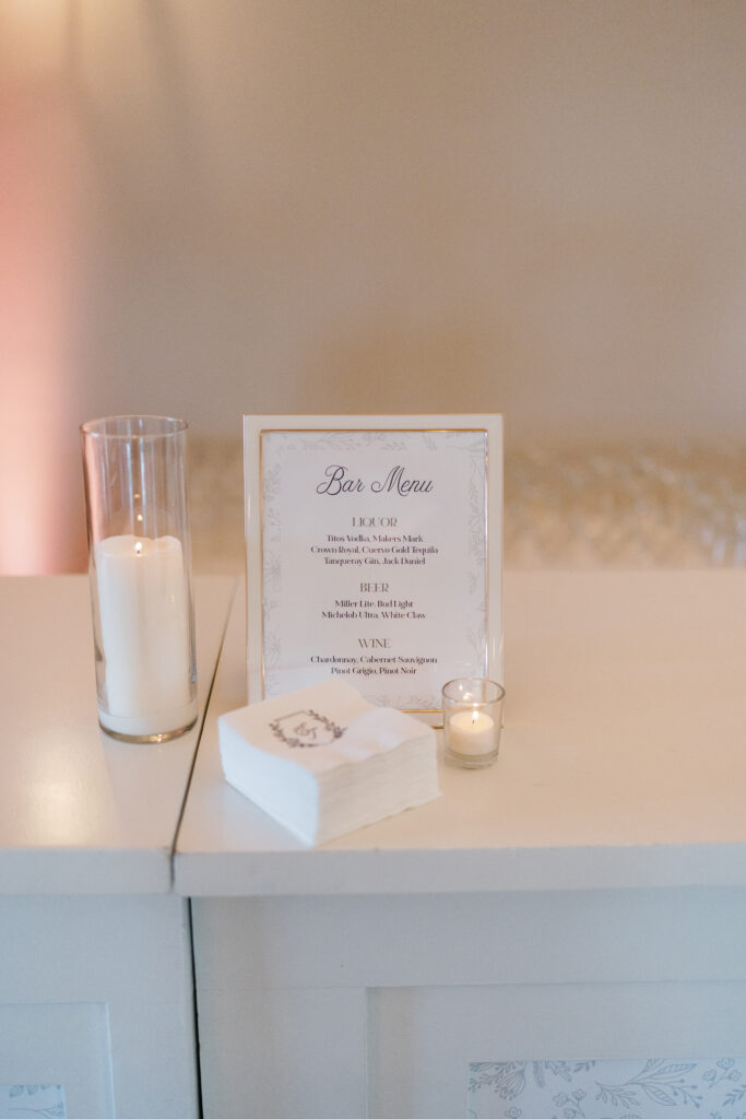 A softly lit bar menu setup featuring elegant signage, custom napkins, and glowing candlelight ambiance.